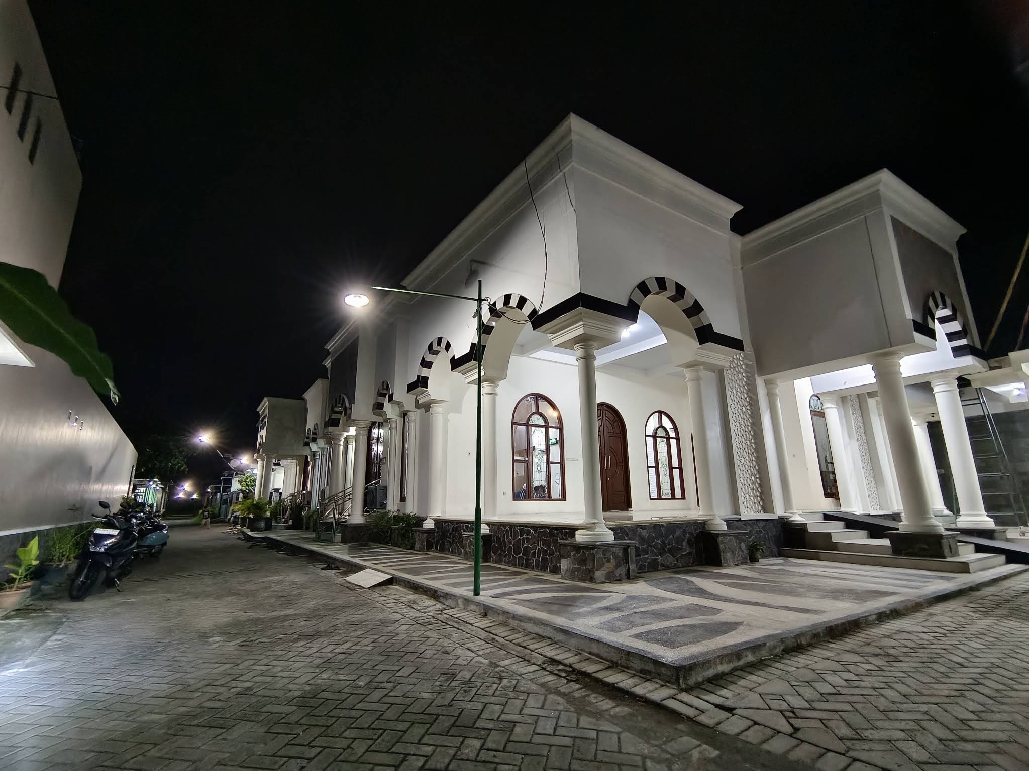 Tampak depan Masjid At Taqwa Sobontoro Indah pada malam hari, dengan pintu dan jendela berbentuk lengkung